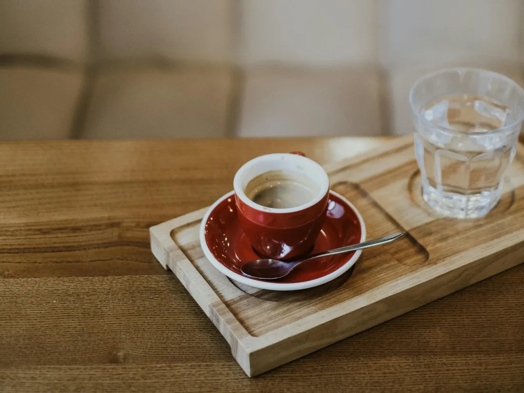 Water and espresso sitting in cups on a wooden table.